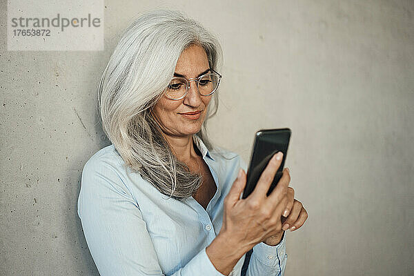 Geschäftsfrau mit Brille und Mobiltelefon vor der Wand