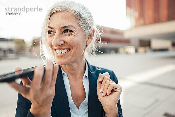 Glückliche Geschäftsfrau  die über den Lautsprecher auf dem Smartphone spricht