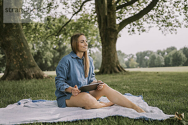 Nachdenkliche Frau mit Tablet-PC sitzt im Park