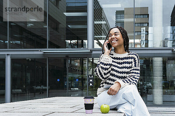 Glückliche junge Geschäftsfrau  die im Büropark mit dem Mobiltelefon spricht