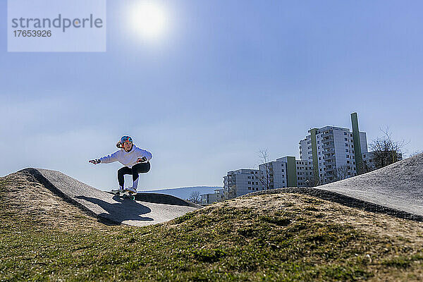 Junge Frau fährt an einem sonnigen Tag Skateboard auf dem Pumptrack