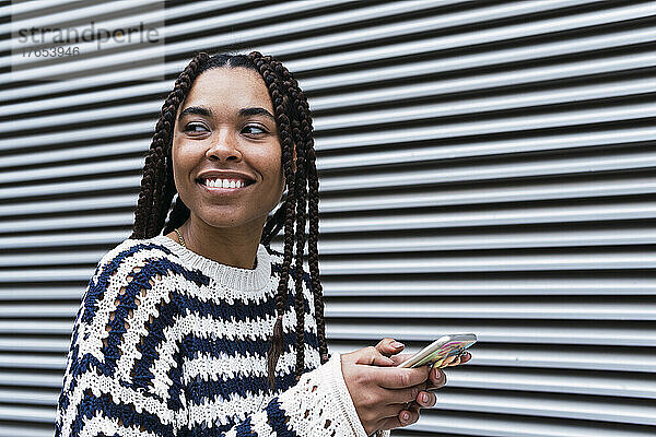Happy businesswoman with mobile phone standing in front of corrugated shutter