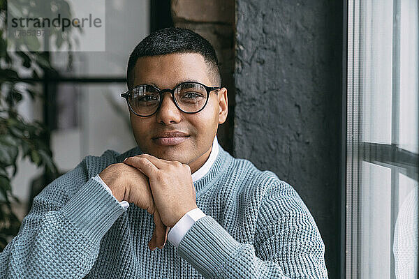 Junger Mann mit Brille am Fenster zu Hause