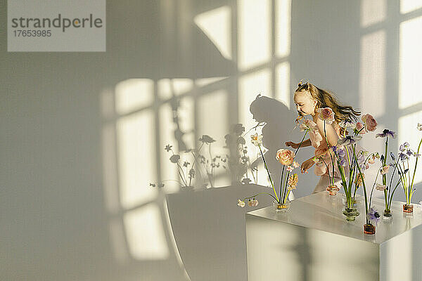 Happy girl running behind table of flowers by white wall