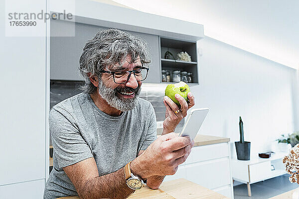 Glücklicher Mann mit Apfel und Smartphone zu Hause