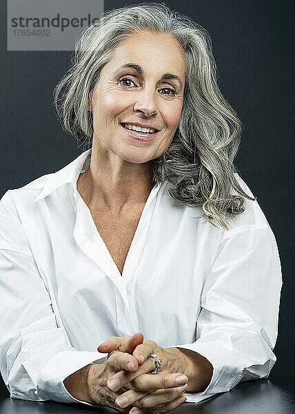 Lächelnde schöne Frau mit grauen Haaren vor schwarzem Hintergrund