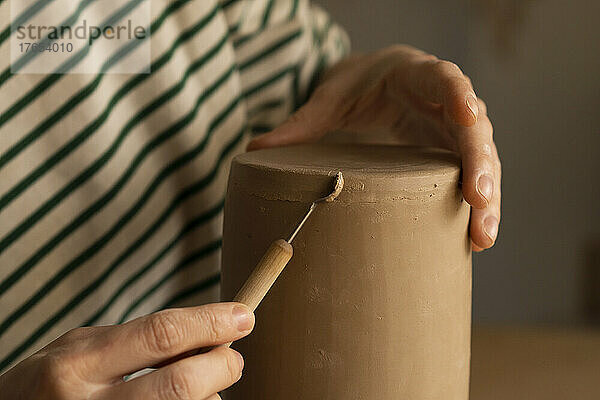 Hände einer Frau  die in der Werkstatt Ton mit einem Handwerkzeug formt