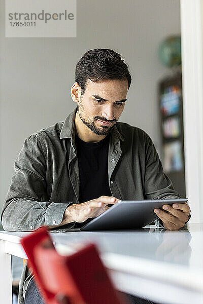 Junger Mann sitzt mit Tablet-PC am Tisch zu Hause