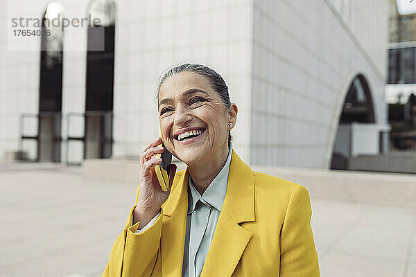 Glückliche Geschäftsfrau  die im Büropark mit dem Smartphone spricht