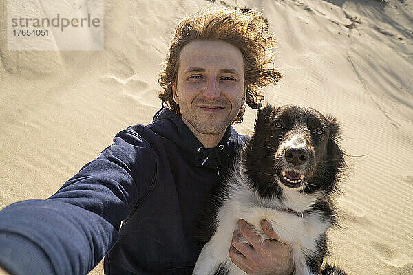 Lächelnder junger Mann  der an einem sonnigen Tag ein Selfie mit seinem Hund macht