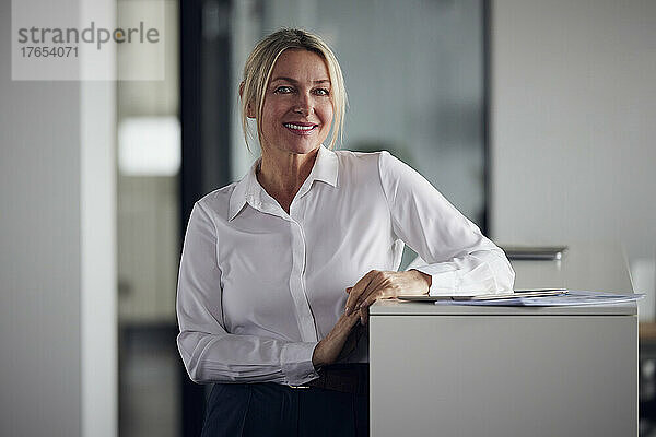 Lächelnde Geschäftsfrau mit Tablet-PC  die neben dem Schrank im Büro steht
