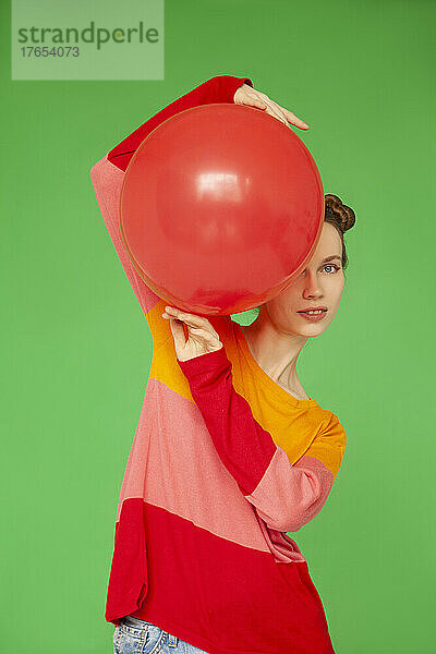 Frau mit rotem Ballon steht vor grünem Hintergrund
