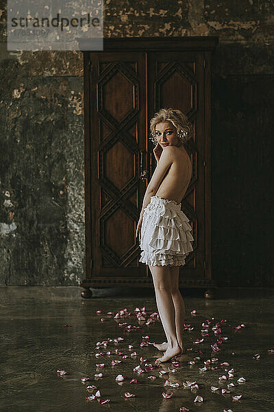 Shirtless young woman standing on flower petals at home