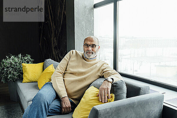 Älterer Mann mit Brille sitzt auf Sofa im Wohnzimmer