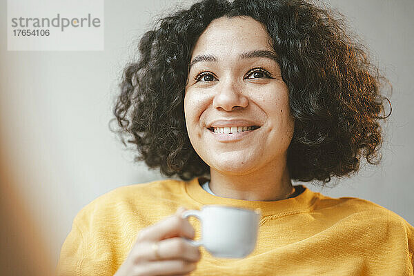 Lächelnde schöne Frau mit lockigem Haar  die eine Kaffeetasse hält