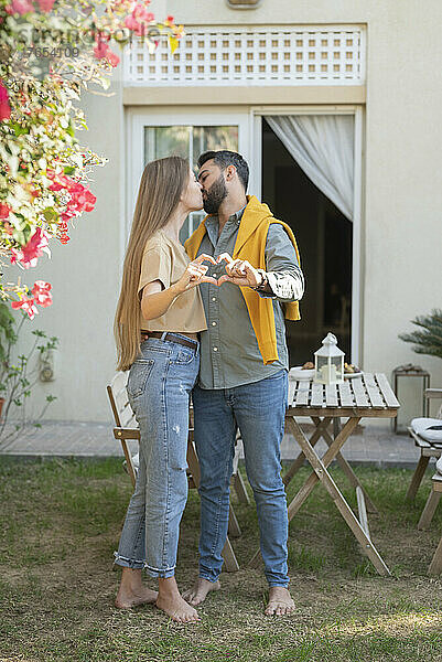 Couple kissing and showing heart sign with hands in back yard garden