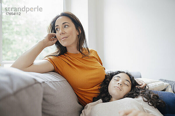 Thoughtful mother with daughter resting on lap at home