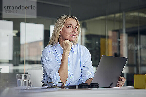 Geschäftsfrau mit der Hand am Kinn am Schreibtisch im Büro