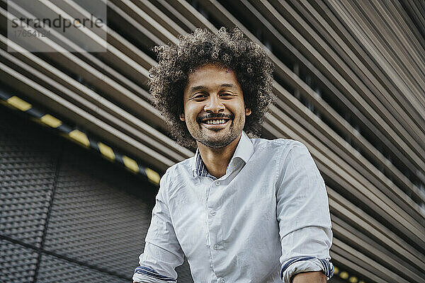 Lächelnder junger Mann vor modernem Gebäude