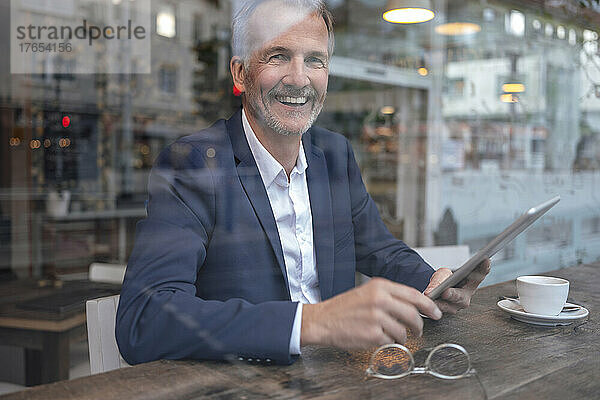 Glücklicher Geschäftsmann mit Tablet-PC  der durch Glasfenster schaut