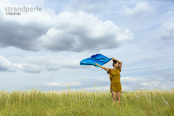 Frau hält windgepeitschten blauen Schal auf der Wiese hoch