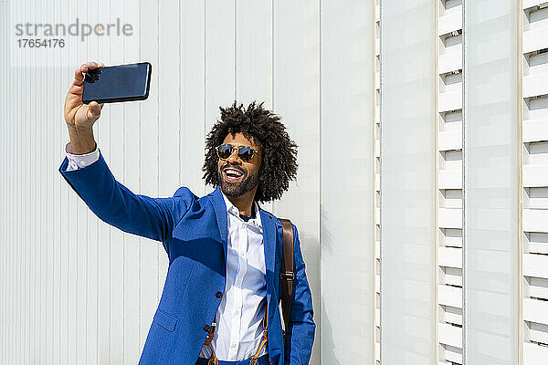 Glücklicher Geschäftsmann  der vor der Wand steht und ein Selfie mit dem Mobiltelefon macht