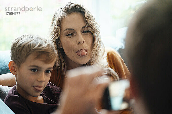 Blonde Frau mit ihrem Sohn  der die Zunge herausstreckt  fotografiert von einem Mann zu Hause