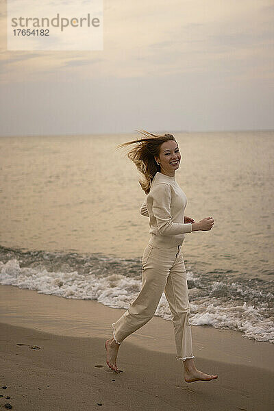 Schöne Frau läuft bei Sonnenuntergang am Strand am Wasser entlang