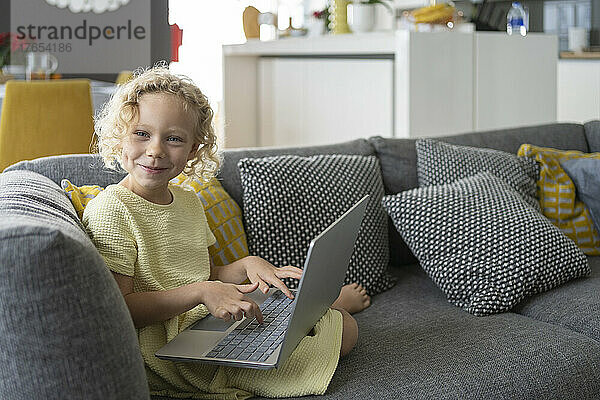 Happy girl with laptop sitting on sofa in living room at home