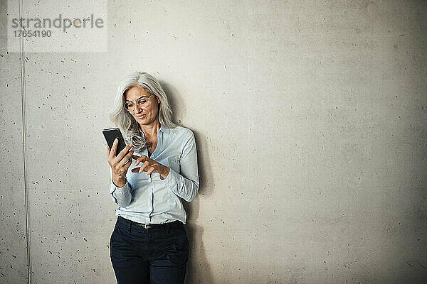 Lächelnde Geschäftsfrau benutzt Smartphone vor der Wand