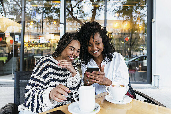 Glückliche Kollegen  die im Straßencafé sitzen und ihr Smartphone teilen