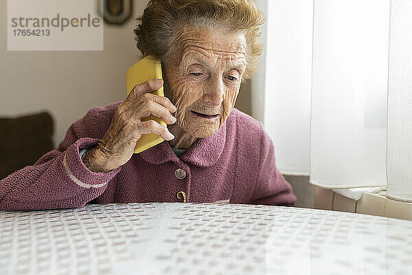 Ältere Frau mit braunen Haaren telefoniert am Esstisch