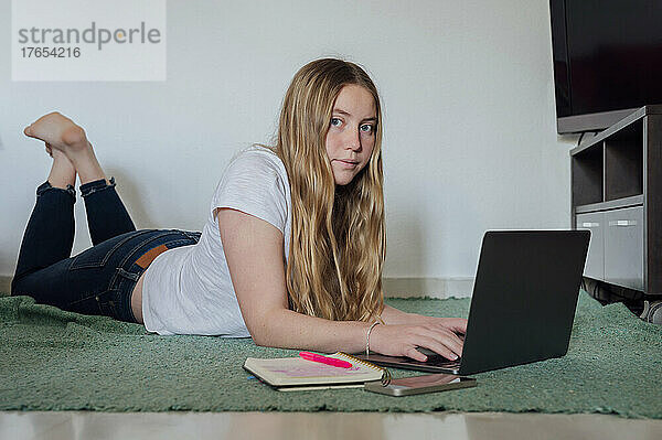 Junge Frau liegt mit Laptop zu Hause
