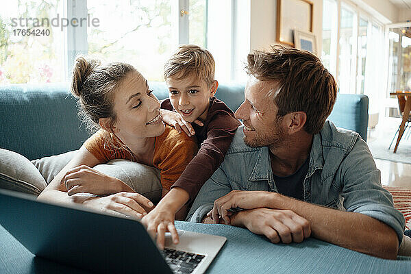 Lächelnder Vater und Mutter schauen den Sohn an  der zu Hause einen Laptop benutzt