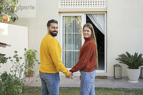 Lächelndes heterosexuelles Paar  das Händchen hält und im Hinterhof steht