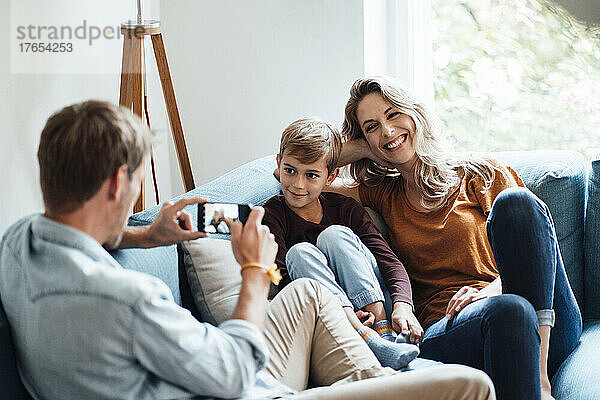 Mann fotografiert Sohn und fröhliche Frau zu Hause per Handy