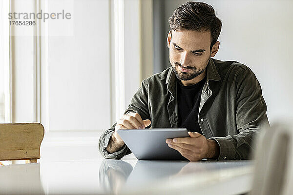 Mann sitzt am Tisch und benutzt zu Hause einen Tablet-PC