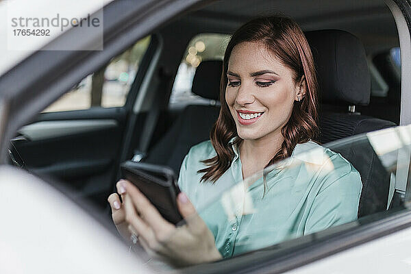 Glückliche Geschäftsfrau benutzt Smartphone im Auto