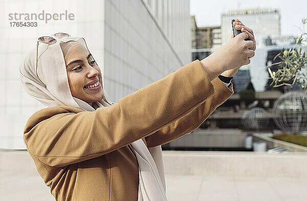 Glückliche junge Frau  die an einem sonnigen Tag im Büropark ein Selfie mit dem Handy macht