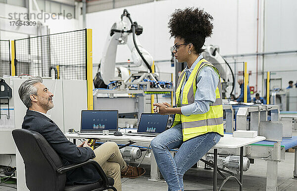 Geschäftsmann diskutiert mit Ingenieur  der am Schreibtisch in der Fabrik sitzt