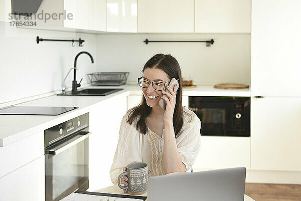 Lächelnder Freiberufler telefoniert mit Laptop in der Küche