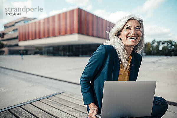 Fröhliche Geschäftsfrau mit Laptop sitzt im Büropark