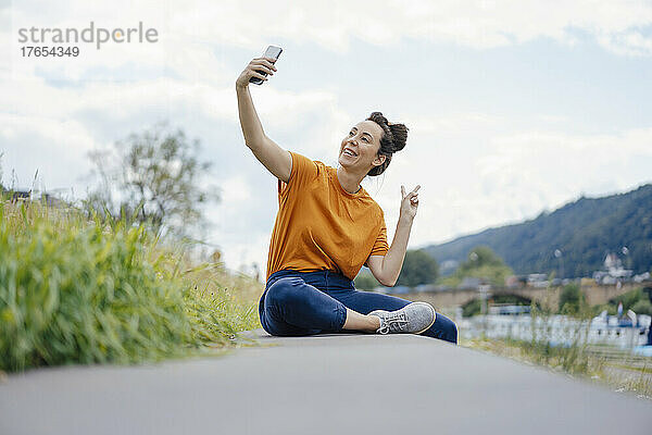 Lächelnde Frau gestikuliert mit Temposchild und macht ein Selfie an der Wand