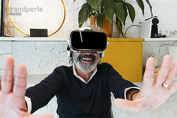 Glücklicher leitender Freiberufler  der einen Virtual-Reality-Simulator trägt und zu Hause gestikuliert