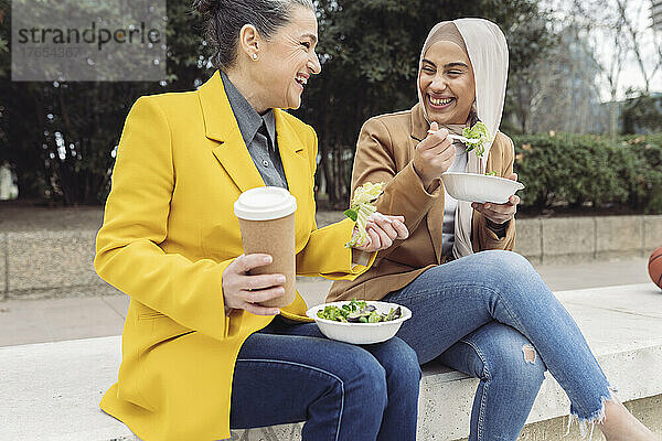 Fröhliche Geschäftskollegen mit Salatschüsseln und Einwegkaffeetasse sitzen auf Stufen