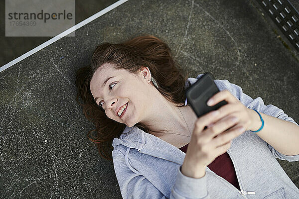 Junge Frau liegt auf einer Tischtennisplatte und hält ihr Smartphone in der Hand