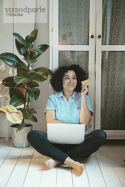 Lächelnde Frau mit Kreditkarte und Laptop beim Online-Einkauf zu Hause