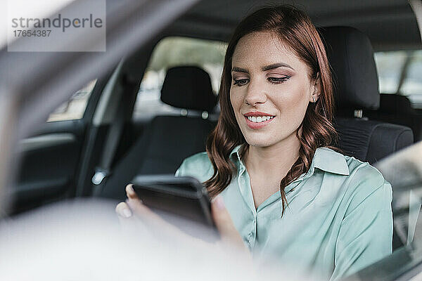 Lächelnde Geschäftsfrau benutzt Smartphone im Auto