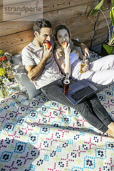 Mann und Frau essen Apfel und ruhen sich auf einer Picknickdecke auf der Terrasse aus