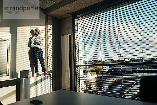 Geschäftsfrau mit der Hand in der Tasche steht auf dem Sideboard im Büro und genießt die Sonne